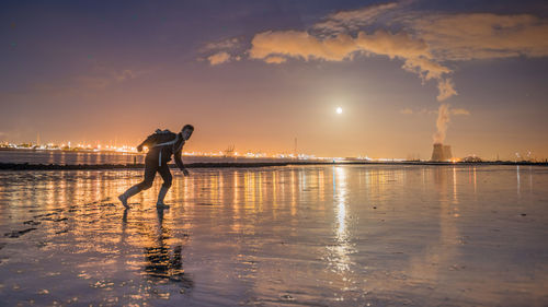 Man standing at beach against sky at dusk