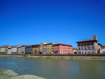 View of buildings by river against blue sky