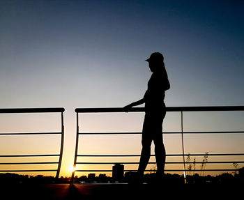 Silhouette woman standing by railing against sky during sunset