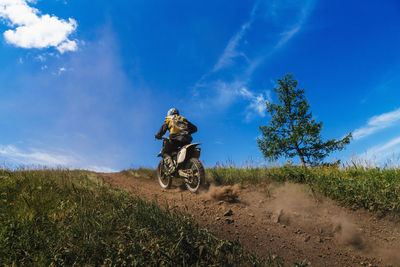 Rear view of man riding bicycle on field against sky