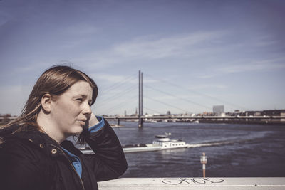 Portrait of young woman looking away at bridge against sky