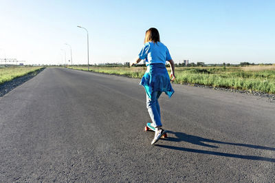 Rear view of woman skateboarding on road