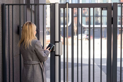 Woman standing near the door and locking it with online application on her smartphone