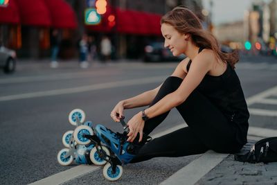 Side view of young woman sitting on street in city