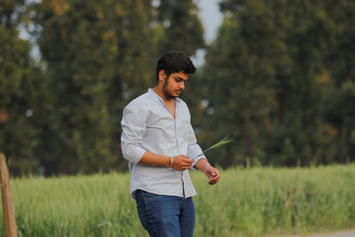 Young man holding wheat while standing on field