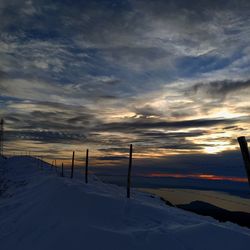 Snow covered landscape against sky during sunset