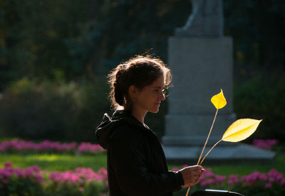 Side view of woman holding leaves standing outdoors