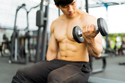 Shirtless male athlete exercising with dumbbells in gym