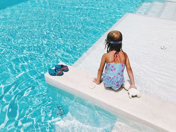 Rear view of girl sitting by swimming pool