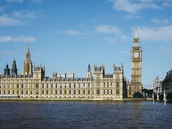 View of clock tower by river against sky in city