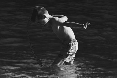 Side view of shirtless boy splashing water in sea