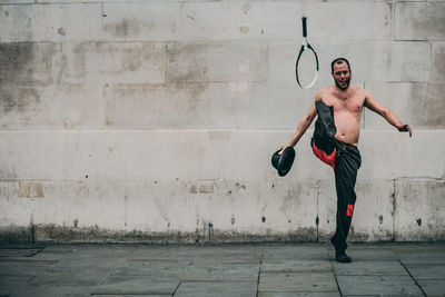 Full length of shirtless man standing against wall