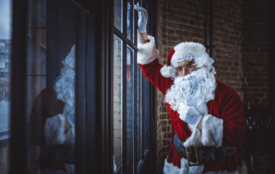 Portrait of man wearing santa claus costume standing by window at home