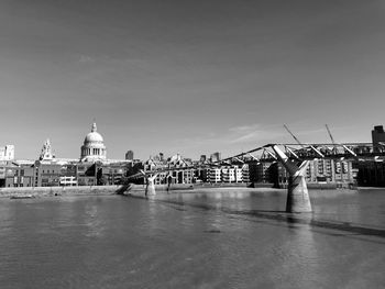 Bridge over river by buildings against sky in city