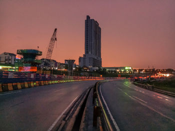 Illuminated city street and buildings against sky during sunset