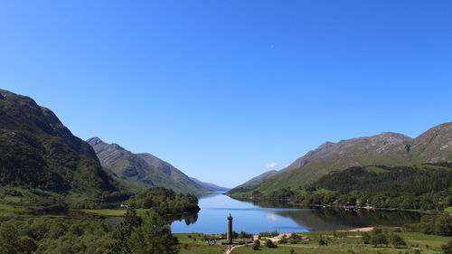 Scenic view of lake and mountains against clear blue sky