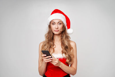 Young woman using phone while standing against white background