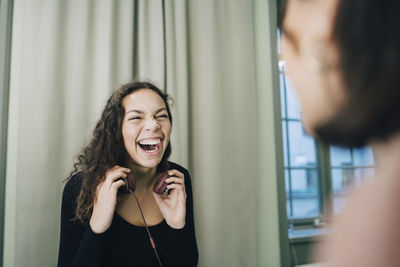 Cheerful teenage girl with headphones looking at female classmate in school