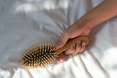 Cropped hand holding hairbrush on bed