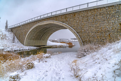 Arch bridge over river against sky during winter