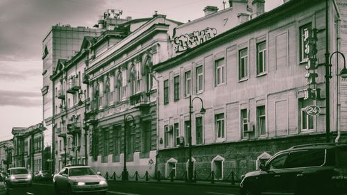 Cars on street by buildings in city against sky