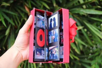 Close-up of hand holding photographs in red gift box