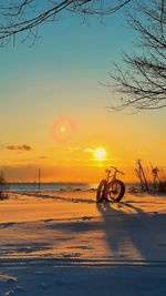 Silhouette bicycle on beach against sky during sunset