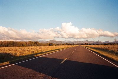 Empty road amidst grassy landscape during sunny day