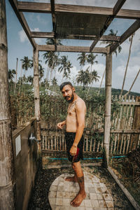 Portrait of shirtless man standing against trees