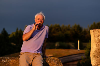 Portrait of man holding electronic cigarette while standing against trees and sky