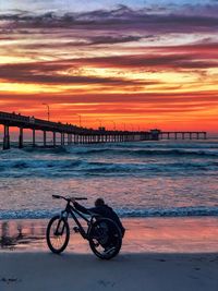 Bicycle on beach against sky during sunset