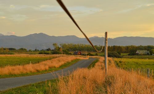 Pole on grassy field by empty road against sky during sunset