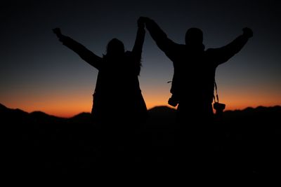 Silhouette people with arms raised against sky during sunset