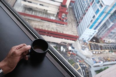 Close-up of hand holding coffee cup on window