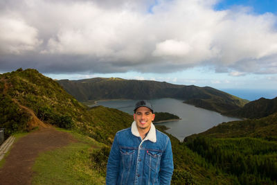 Portrait of smiling young man standing on mountain against cloudy sky