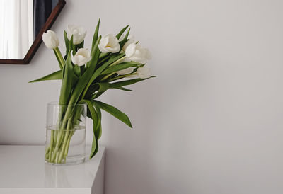 White tulips in the vase over the white wall. home decor