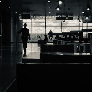 Silhouette people standing by glass window at airport