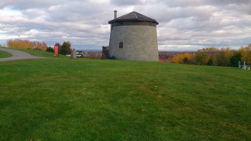 Tower on grassy field against cloudy sky