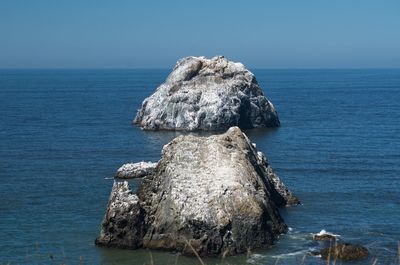 Rock formation in sea against clear blue sky