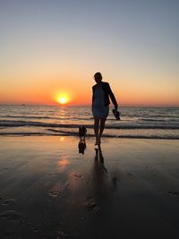 Man with dog on beach during sunset