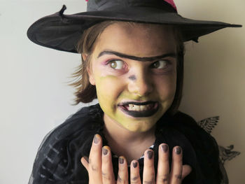 Girl wearing witch costume and hat clenching teeth standing against wall at halloween