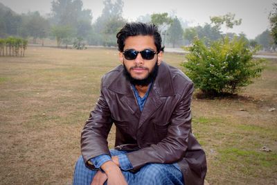 Young man wearing sunglasses while sitting on field