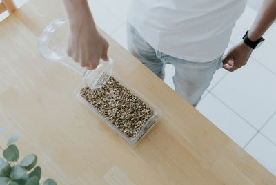 A young man waters wheat seeds into a container.