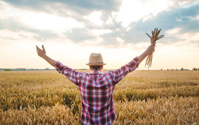 Rear view of man with arms outstretched standing at wheat farm-