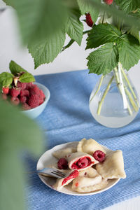 Slavic dish vareniki with fresh raspberries, still life on a blue background with a bouquet 