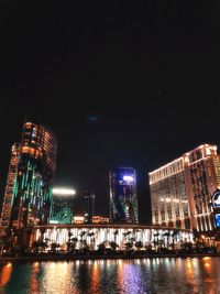 Illuminated buildings by river against sky at night