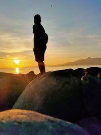 Silhouette man standing on rock against sky during sunset