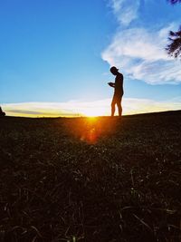 Silhouette man standing on field against sky during sunset