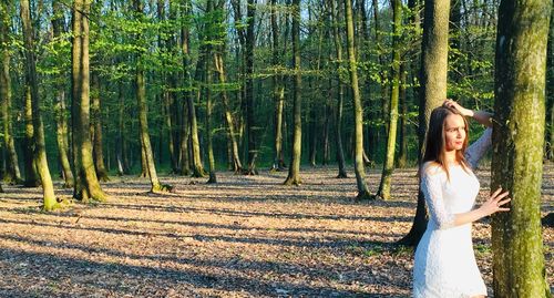 Woman standing by tree trunk in forest