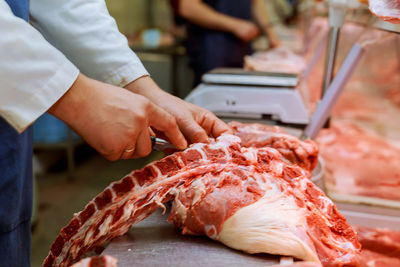 Midsection of butcher cutting meat on table at shop